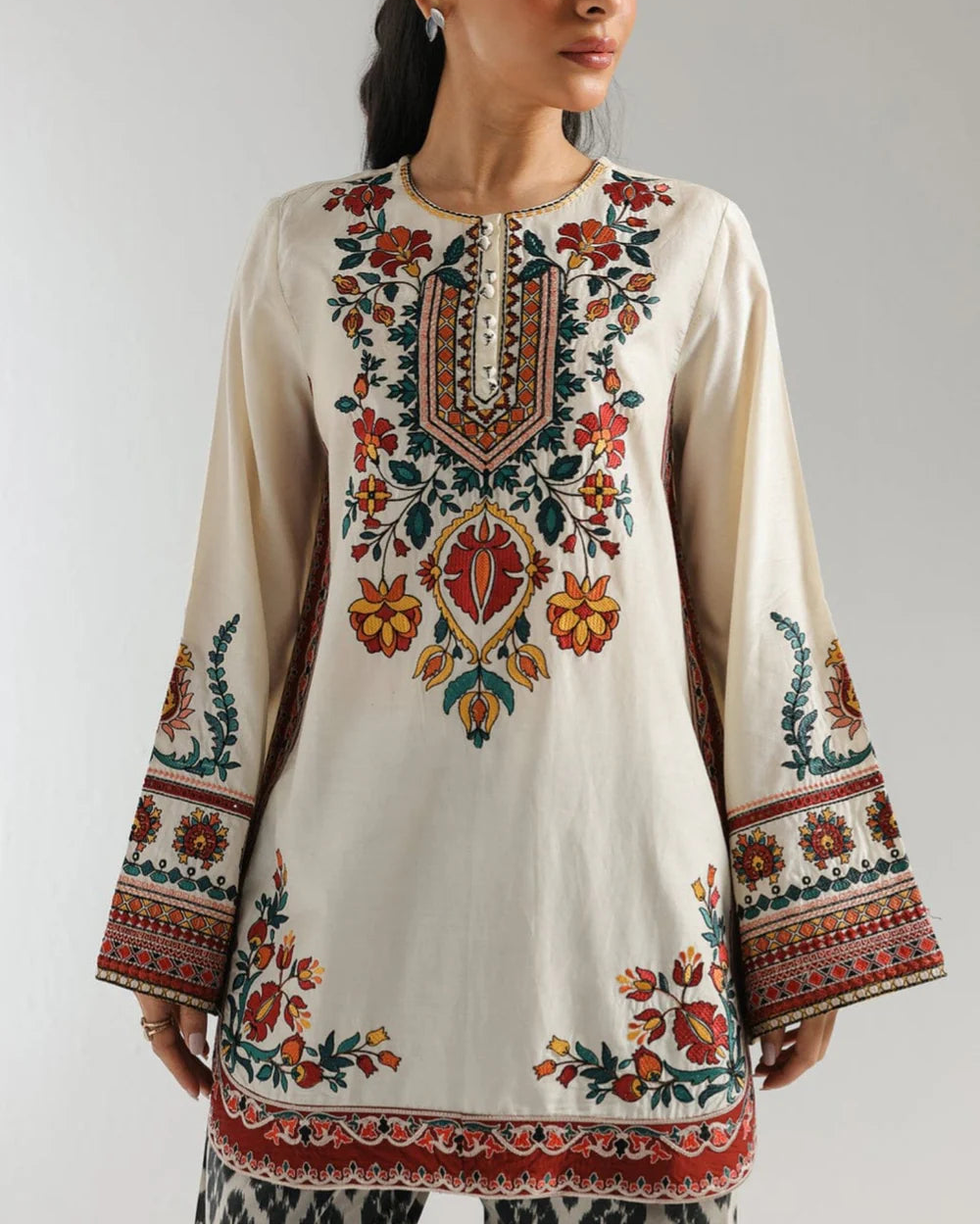 Woman wearing a traditional embroidered outfit with a plain background